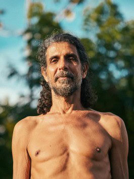Robin Mellor - Portrait of a shirtless man with long hair and beard outdoors, natural setting, sunlight, greenery. 