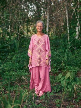 Woman in pink traditional dress smiling in a natural garden setting. 