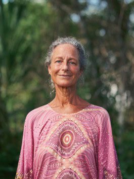 Elder woman smiling outdoors, surrounded by lush greenery, showcasing vitality and wisdom. 