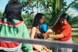 Woman being baptized in outdoor water ceremony with community members present.