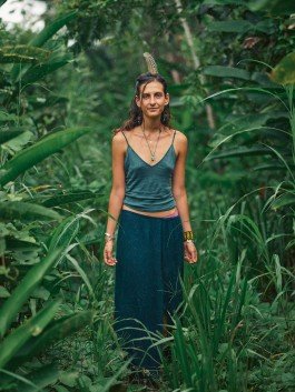 Woman standing amidst dense jungle foliage, dressed in bohemian style with feathers and jewelry. 