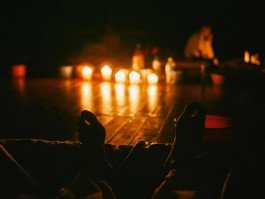 Robin Mellor performing in a dimly lit setting with candles and a person in the background. 