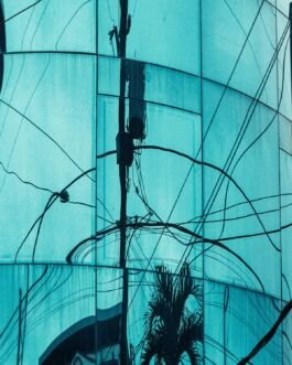 Electric pole with wires reflected on a modern glass building facade. 