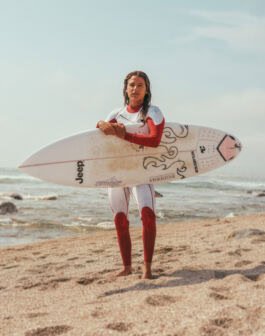 Surfing woman with surfboard on sandy beach, ocean and sky in background, sunny weather. 