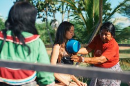 Woman being baptized in outdoor water ceremony with community members present. 