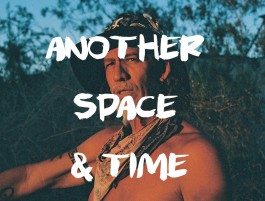 Indigenous man with traditional attire outdoors, nature background. 
