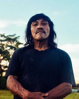 Portrait of a confident man with long black hair outdoors against a blue sky. 