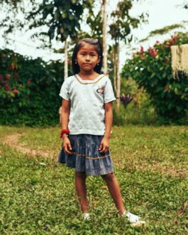 Young girl in casual clothing standing in a garden with lush greenery and flowering plants. 