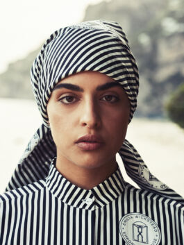 Close-up portrait of a woman wearing a black-and-white striped headscarf and shirt with a circular emblem on the chest. 