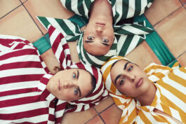 Four people lying in a circle on a tiled floor, wearing bold red, green, and yellow striped outfits. 